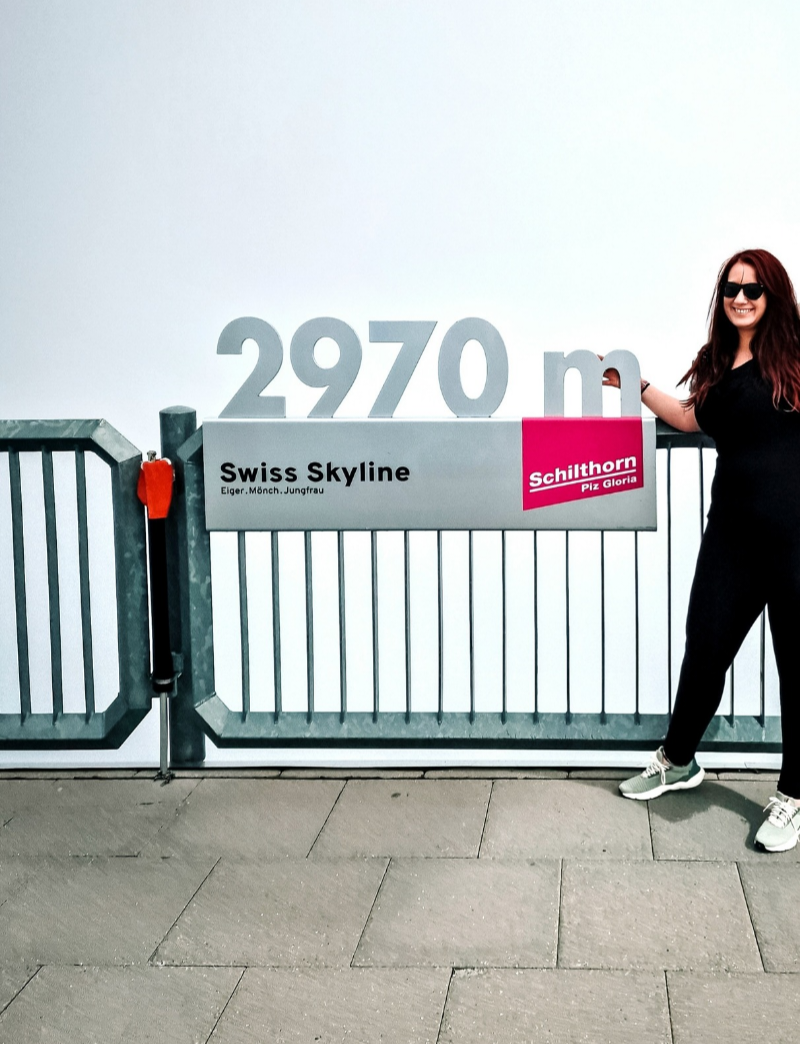 Myself posing next to the "2970m Swiss Skyline" sign on the Schilthorn viewing platform. The clouds have completely covered the sky so there is only a white background.