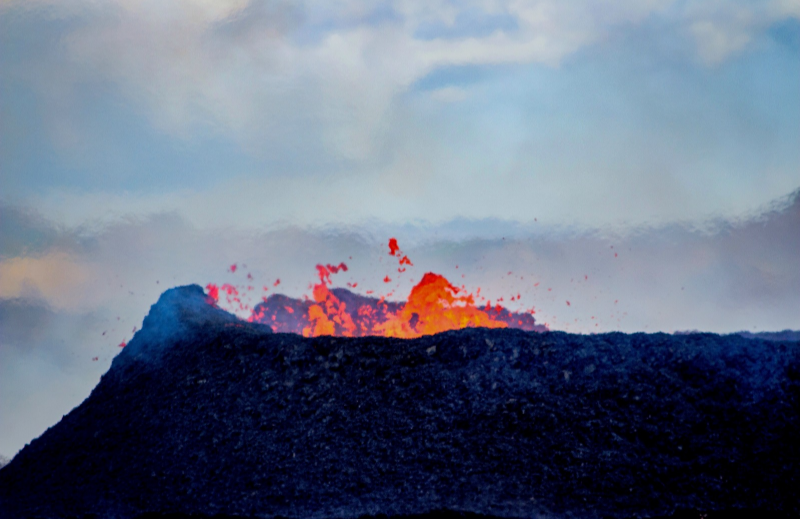 A close-up image of the active crater from the Litli-Hrútur (July 2023) eruption in Fagradalsfjall. There is some orange lava spewing over the top; the texture of the crater and the surrounding heatwaves can also be seen.