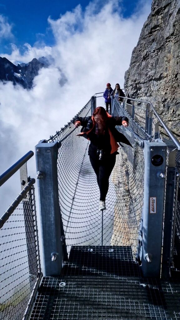 A snapshot of myself walking across the 9m tightrope walk over the side of the Schilthorn mountain. There is a metal casing around the tightrope for safety.