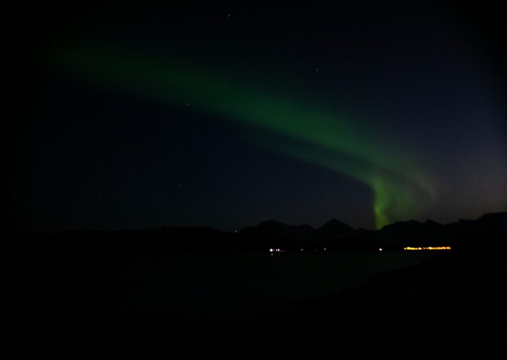 An image of the Aurora streaking across the dark sky, right about the darkened mountain peaks.